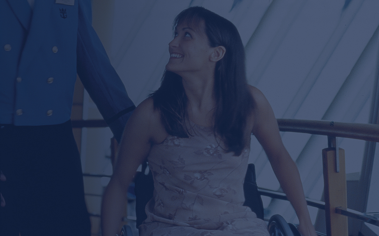 A girl in a wheelchair receiving assistant from a Royal Caribbean Cruise Line employee onboard the ship.